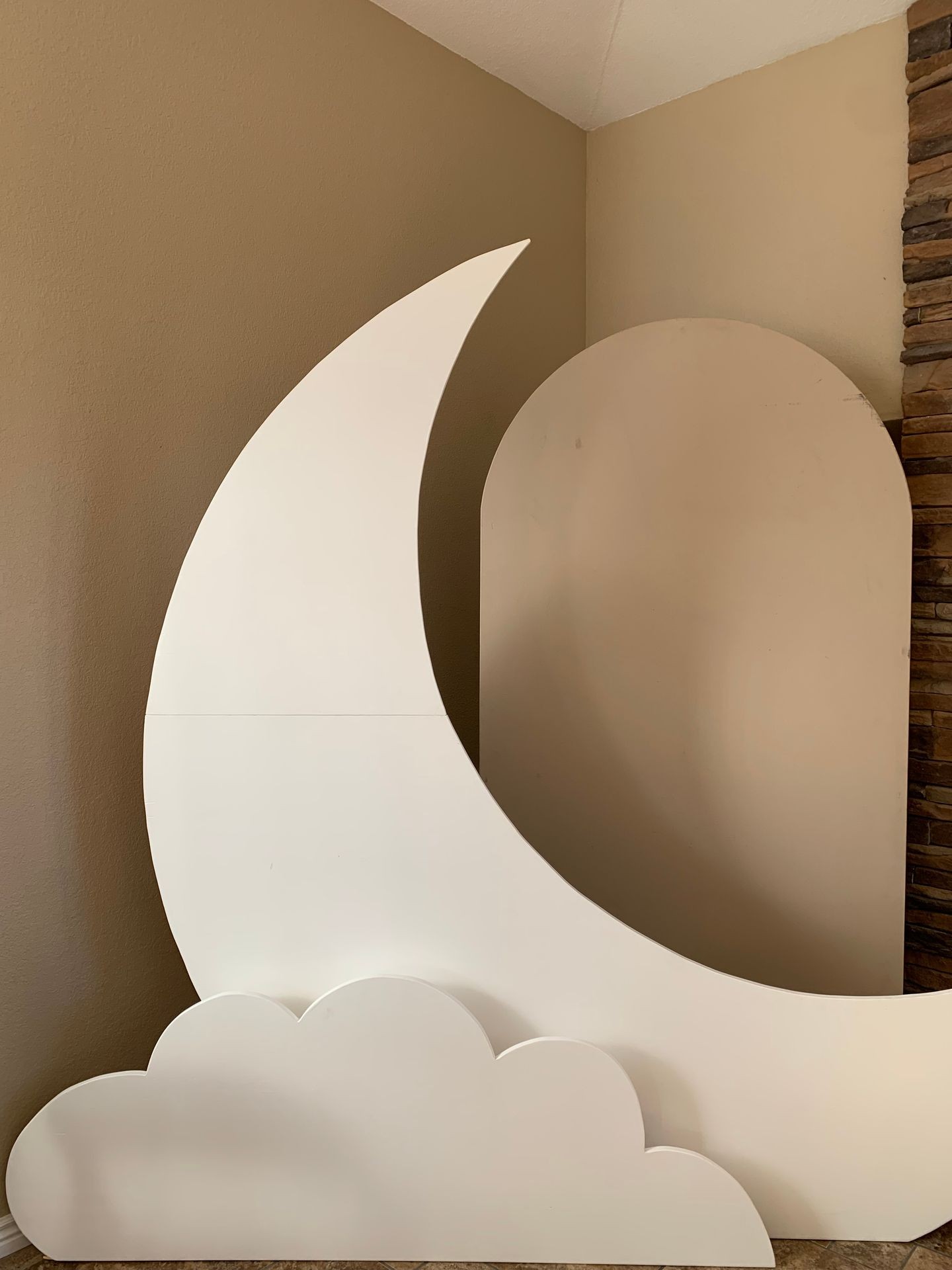 Decorative white cardboard cutouts resembling a crescent moon and clouds placed against a tan wall.