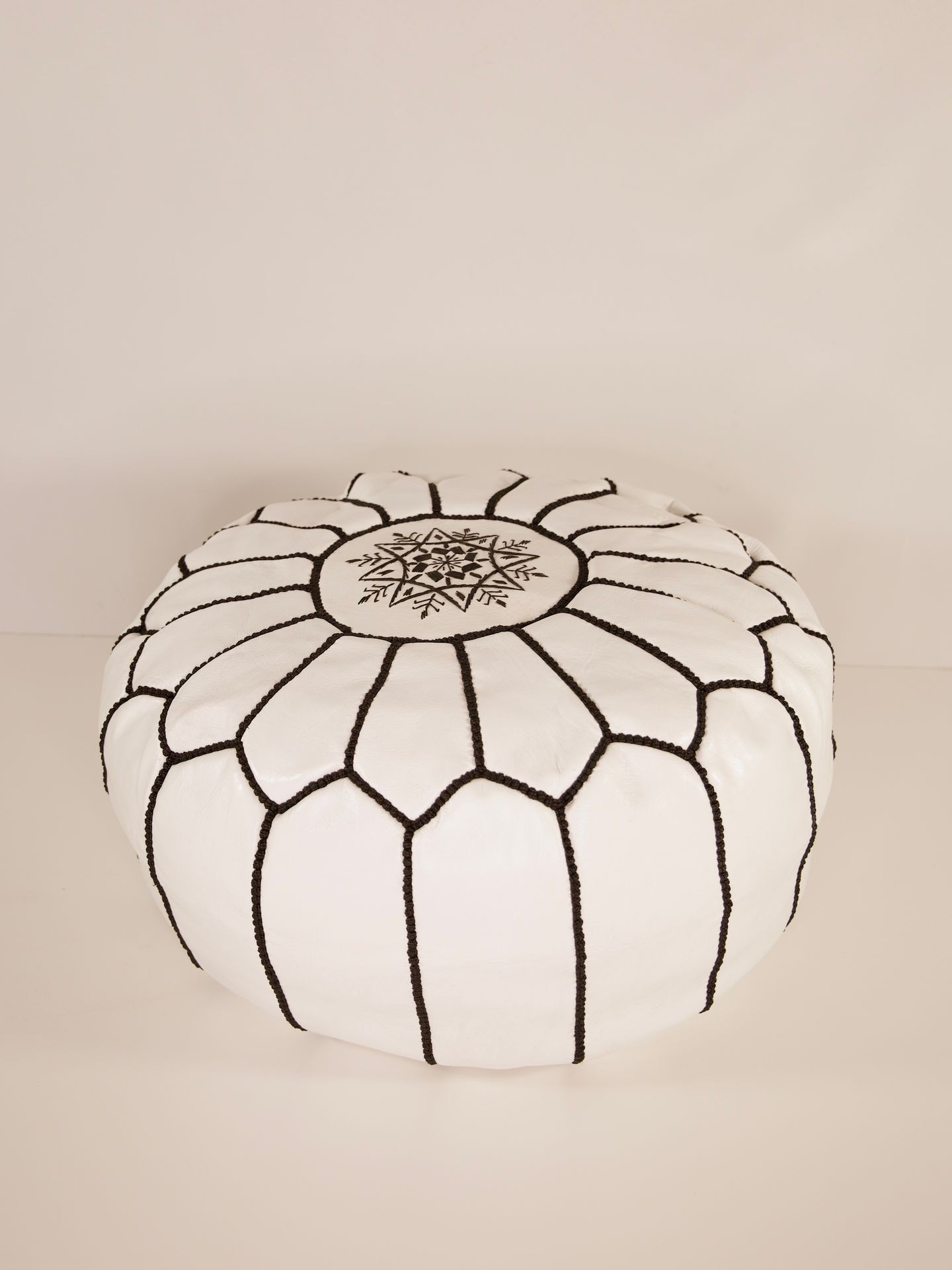 White round pouf ottoman with black geometric stitching and an intricate central pattern.