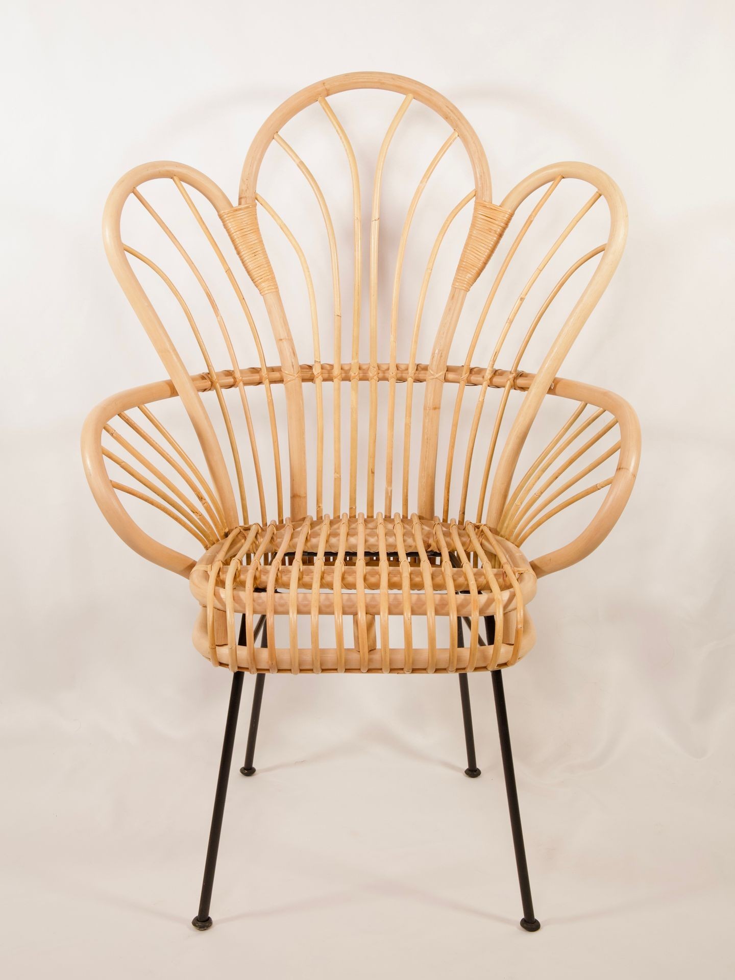 A stylish wicker chair with a unique and intricate backrest design, supported by black metal legs.