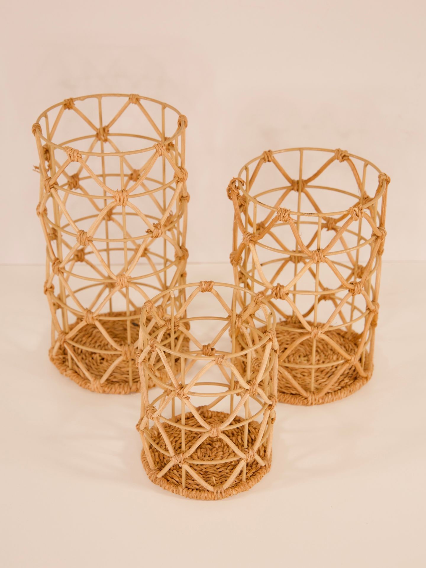 Three woven rattan cylindrical baskets of varying sizes placed on a light background.