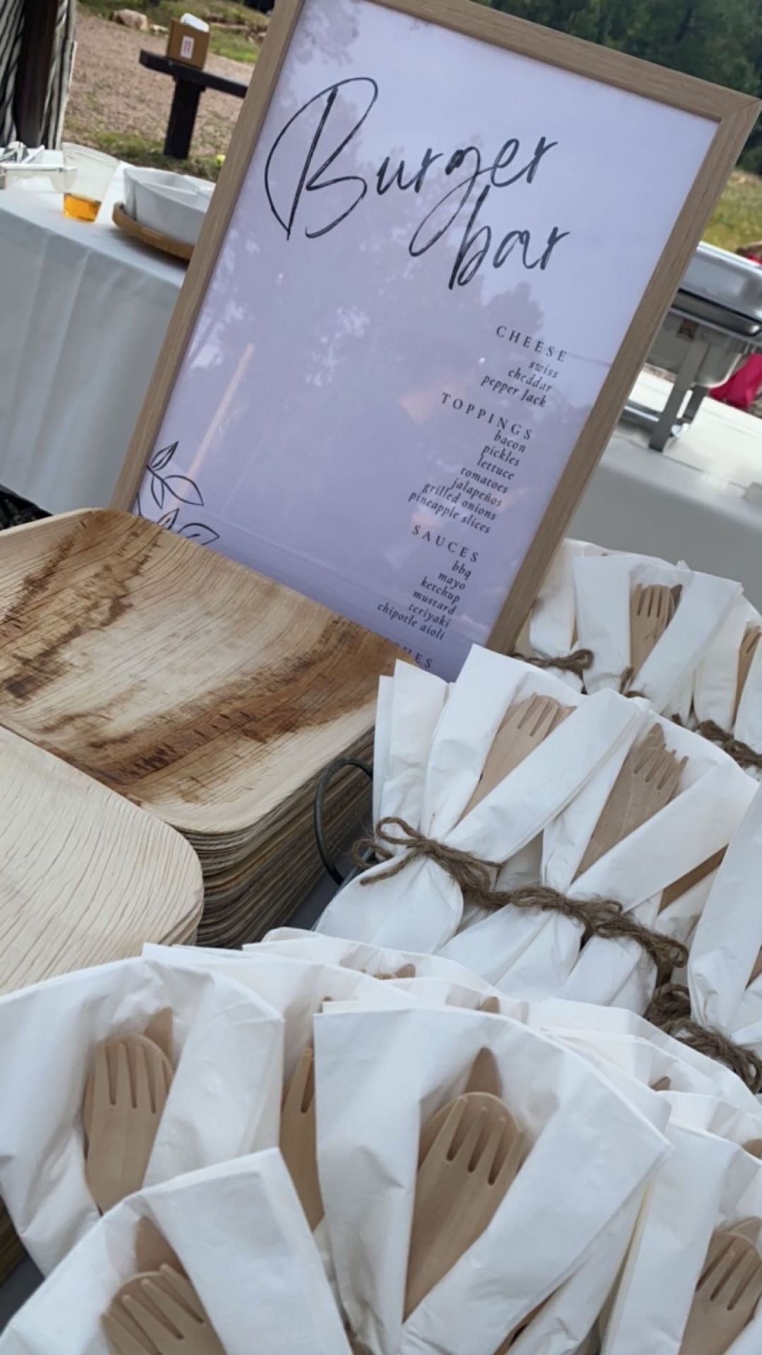 A burger bar setup with a menu, wooden plates, and wrapped utensils displayed on a table.