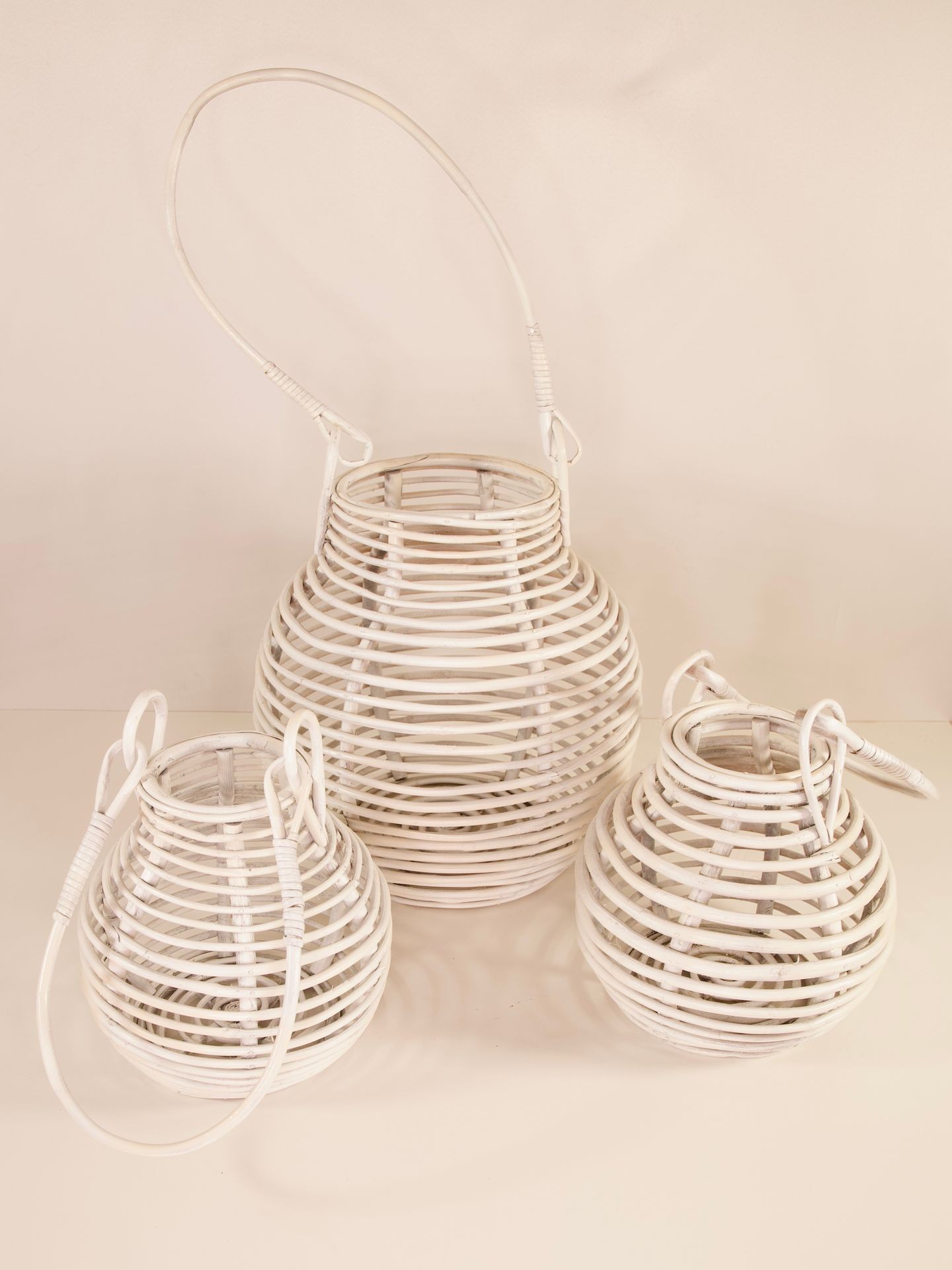 Three white wicker lanterns of different sizes with handles, arranged on a light background.