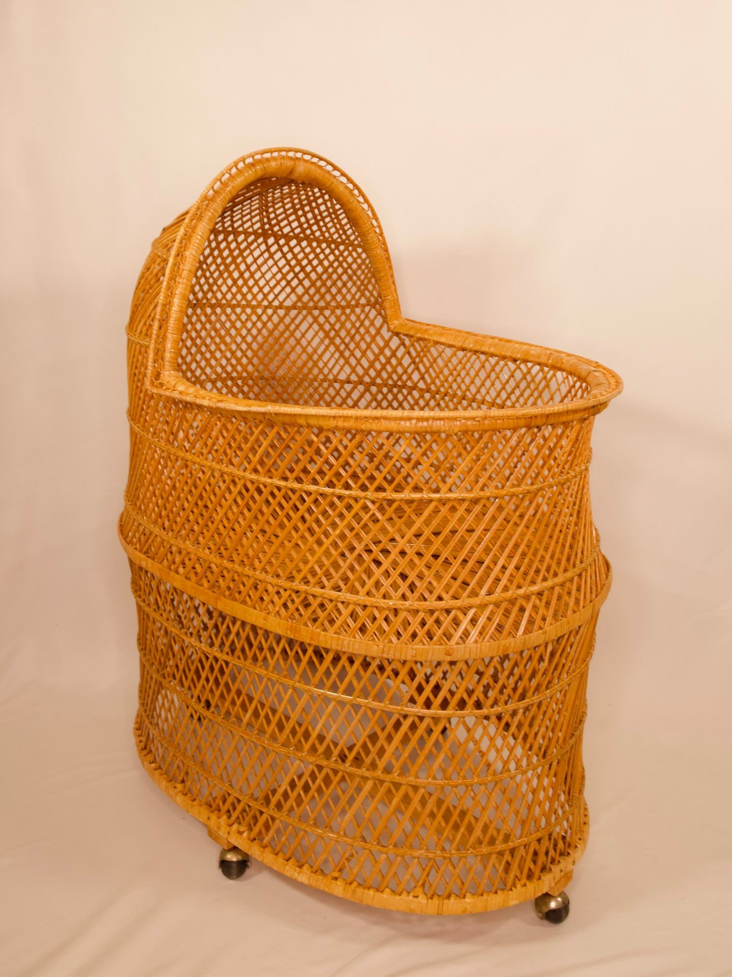 Vintage wicker bassinet with an arched, enclosed hood on small wheels against a plain background.