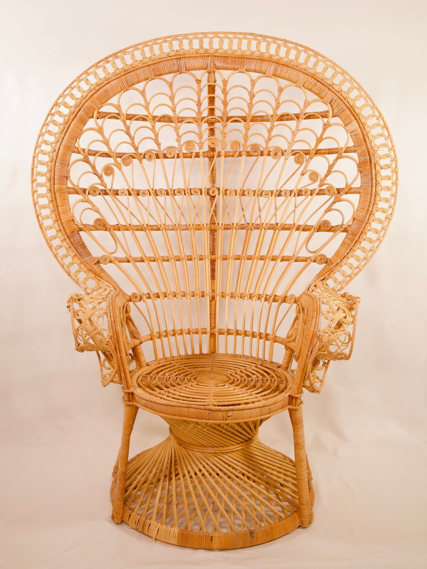 Vintage wicker peacock chair with intricate design and circular backrest on a plain background.