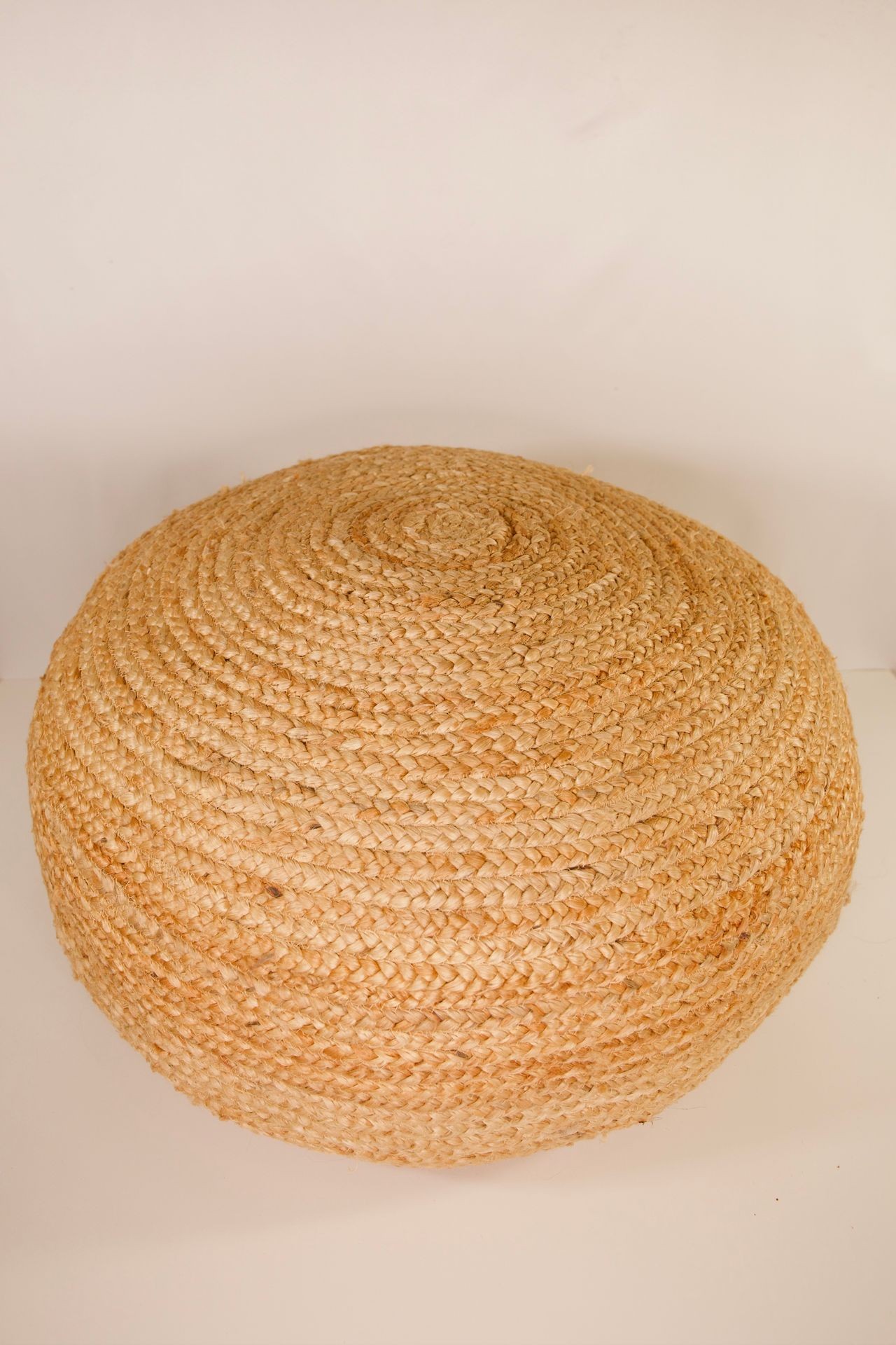 Round woven straw pouf with natural fibers placed on a light background.