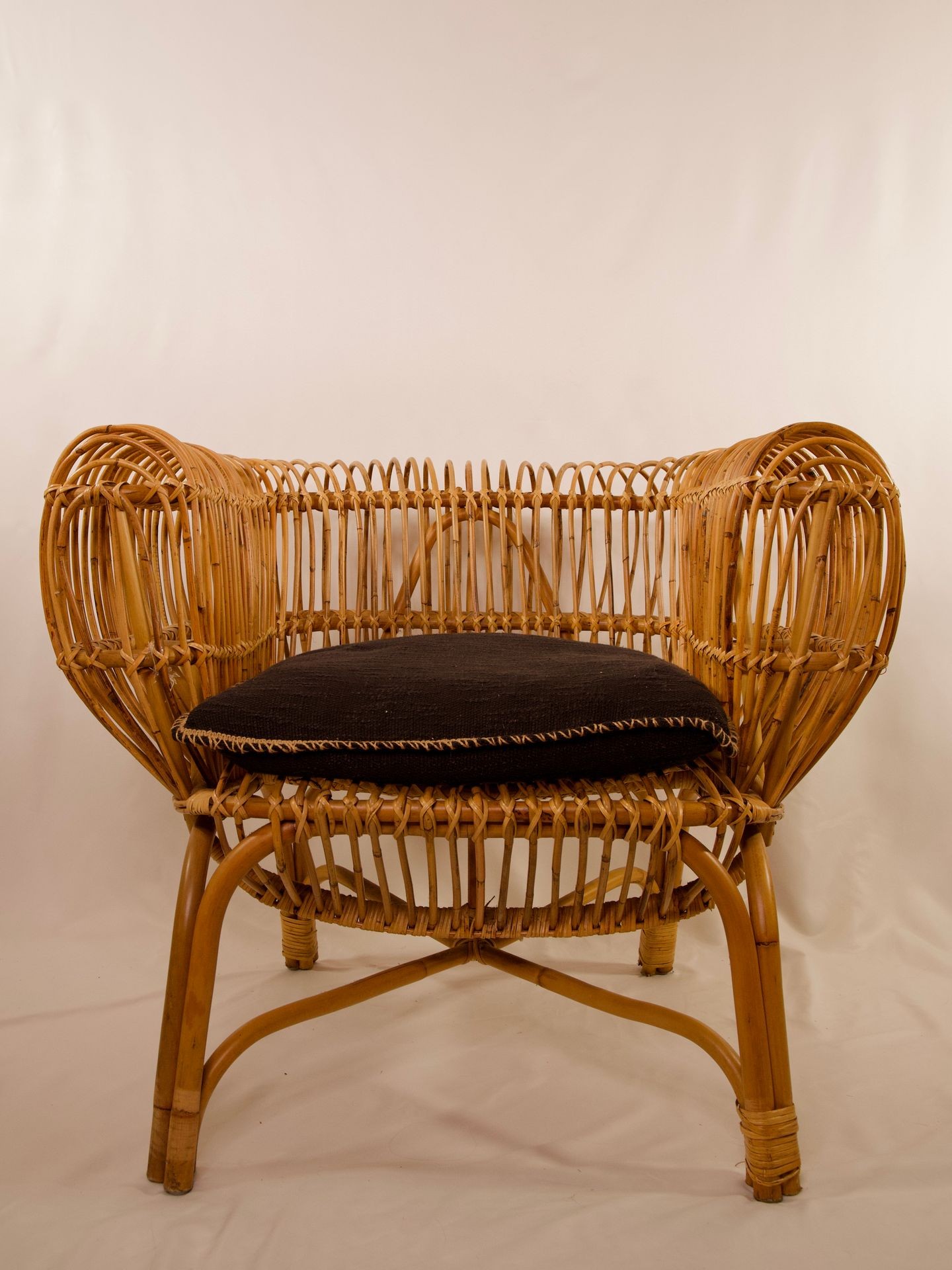 Wicker chair with a curved design and black cushion seat set against a plain background.