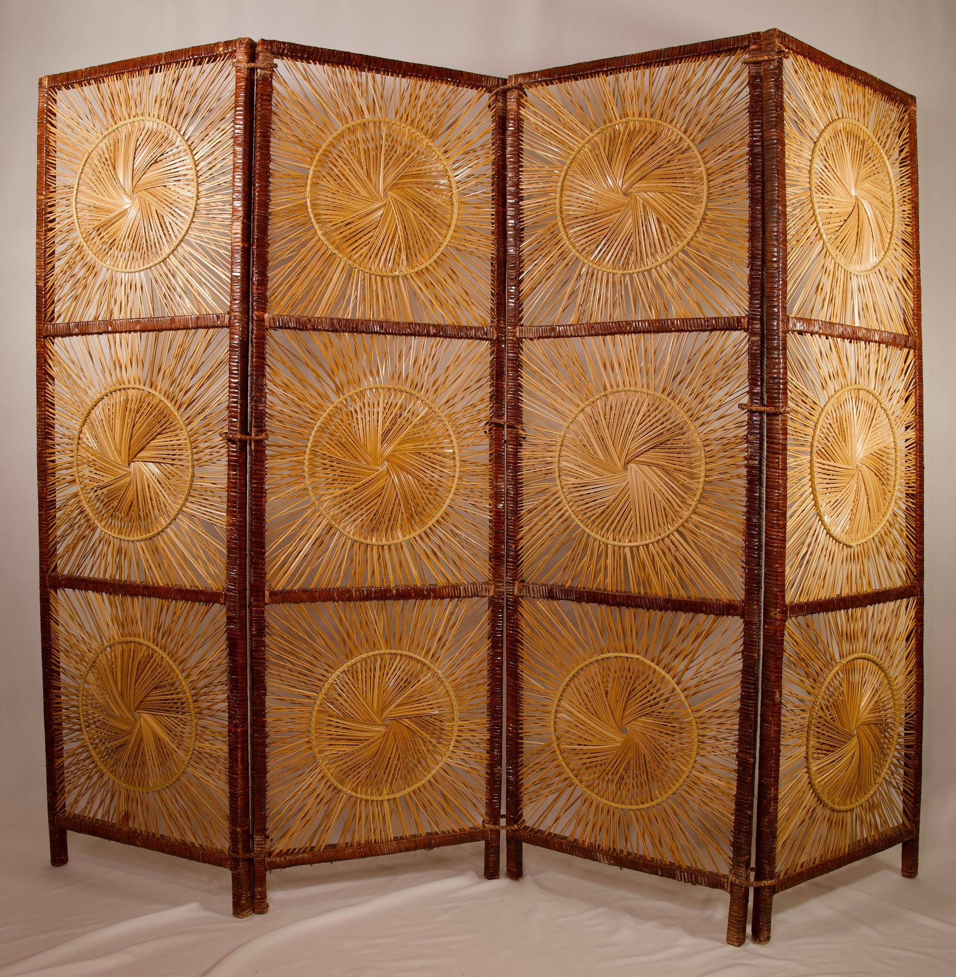 Foldable room divider with woven rattan panels featuring sunburst designs.