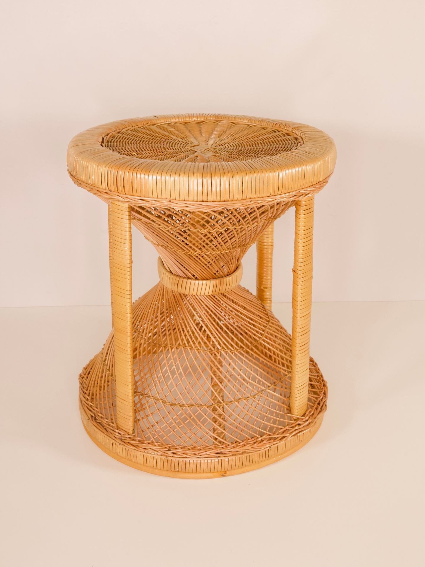 A woven rattan stool with a round seat and intricate, hourglass-shaped base design.