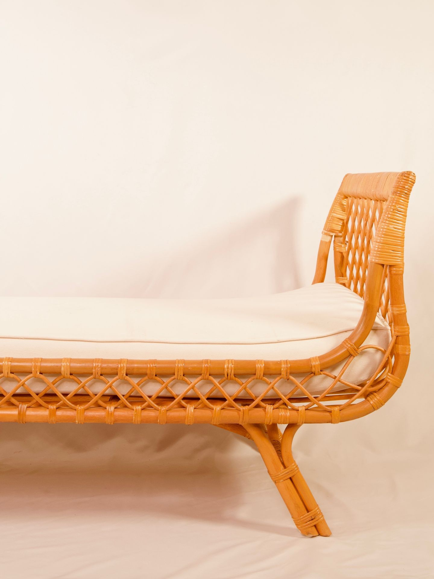 Close-up view of a wicker chair with a cushioned seat against a soft beige background.