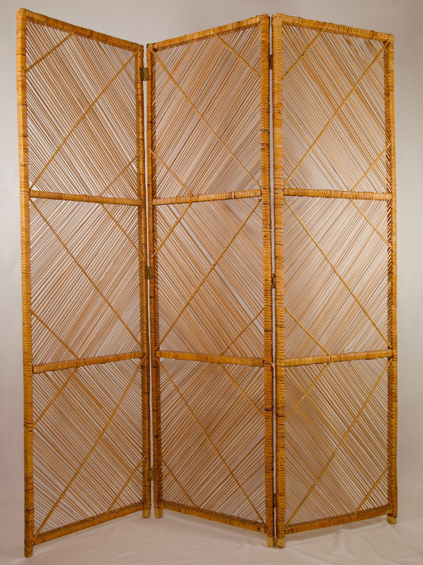 Three-panel folding room divider made from woven natural materials, featuring a geometric crisscross design.