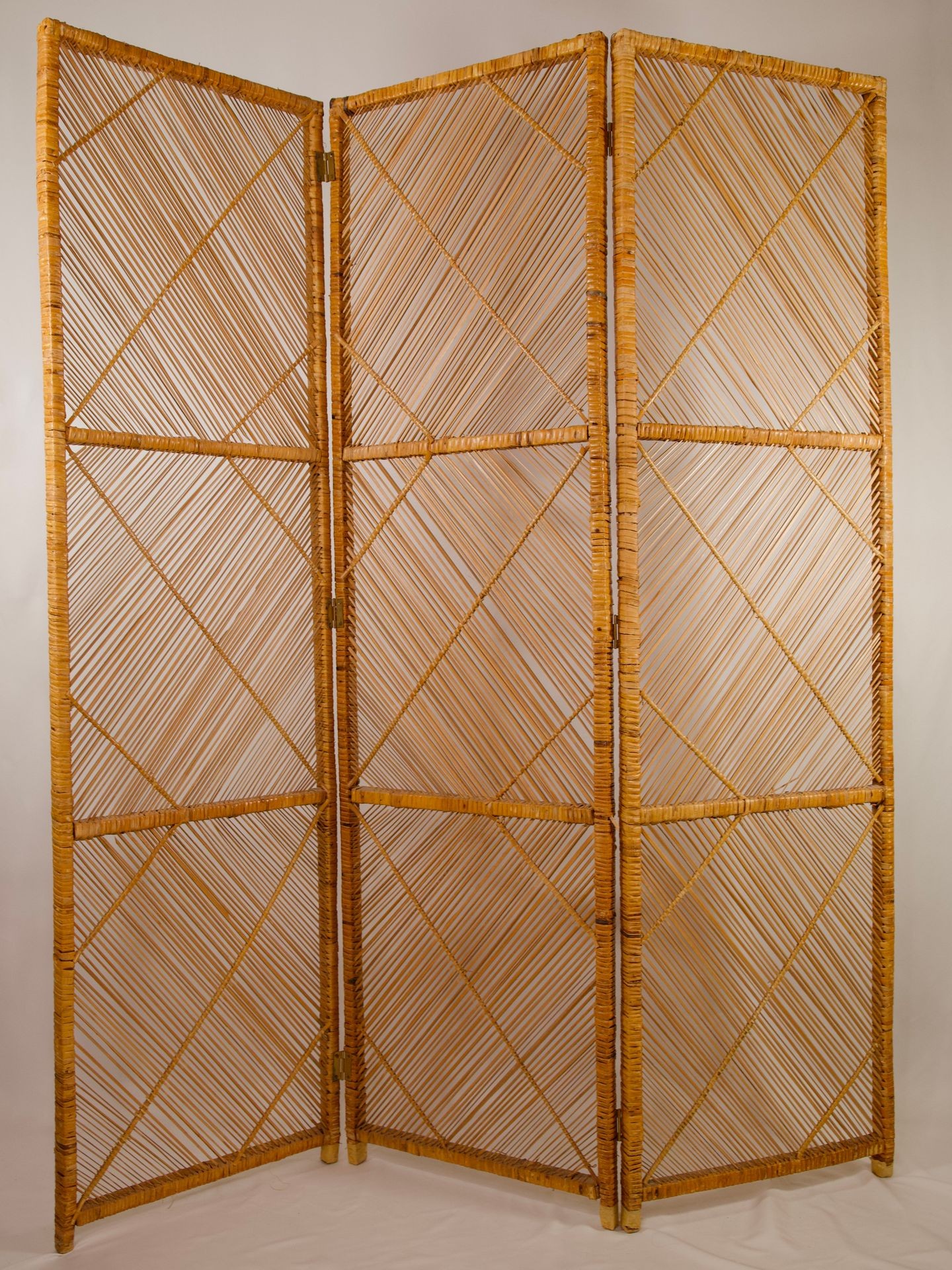 Three-panel folding room divider made from woven natural materials, featuring a geometric crisscross design.