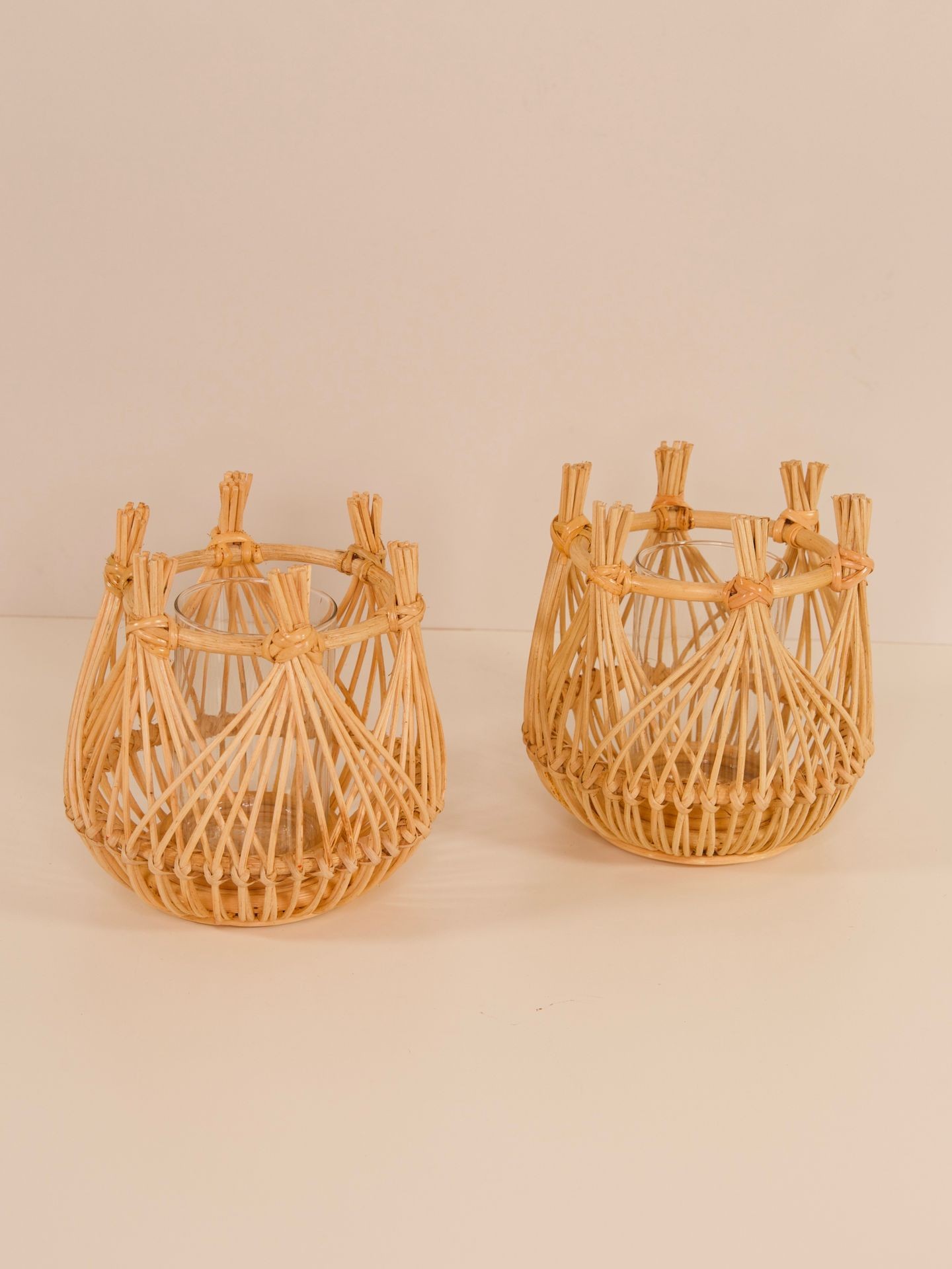 Two empty wicker lantern candle holders placed on a beige surface against a matching wall.