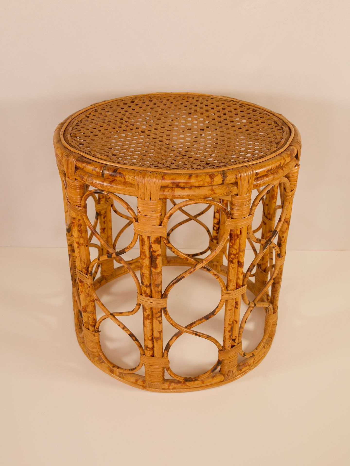 Round wicker side table with a woven top and intricate openwork design on the sides.