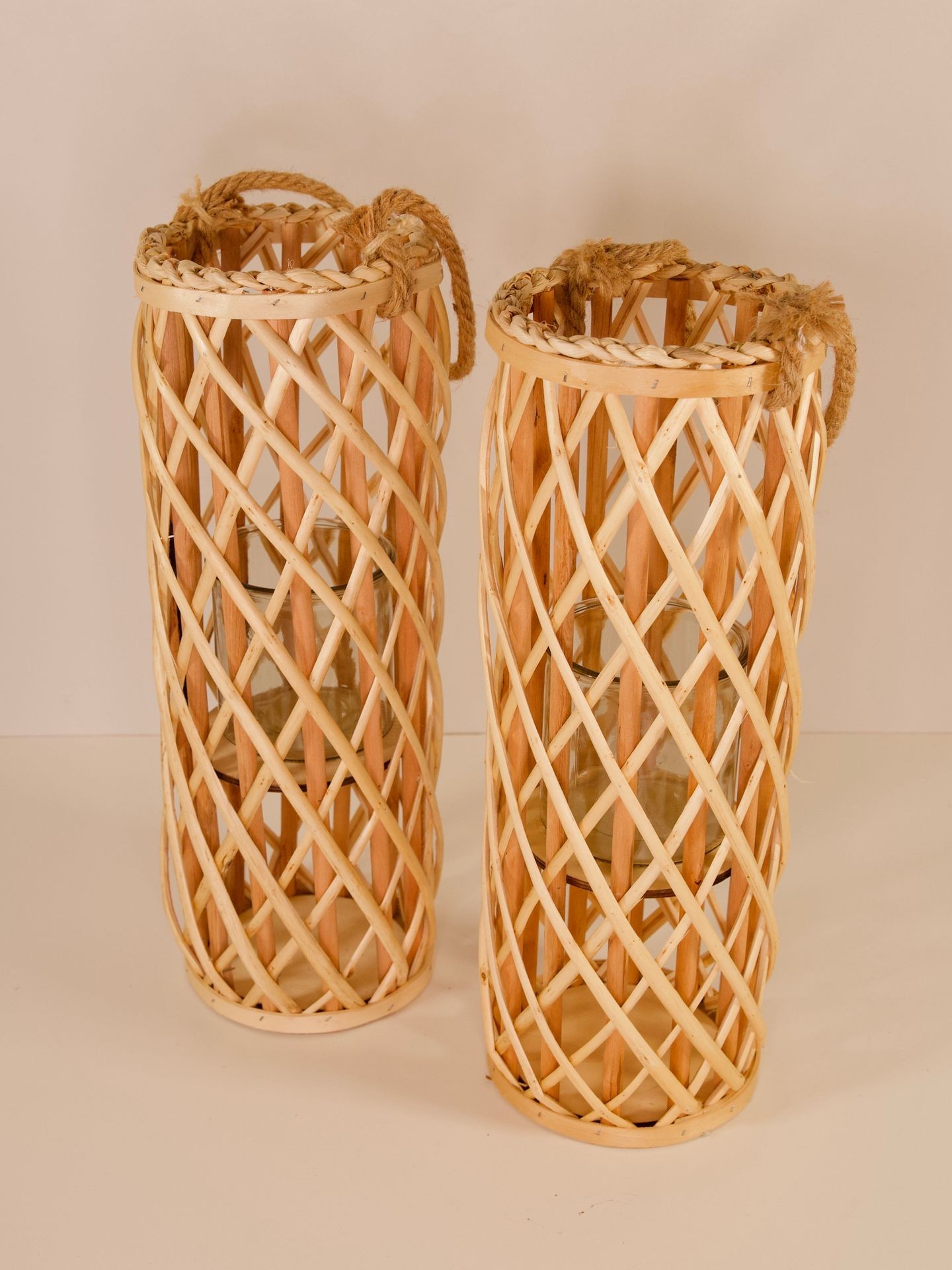 Two large wicker lanterns with woven bamboo patterns and rope handles, standing on a beige surface.