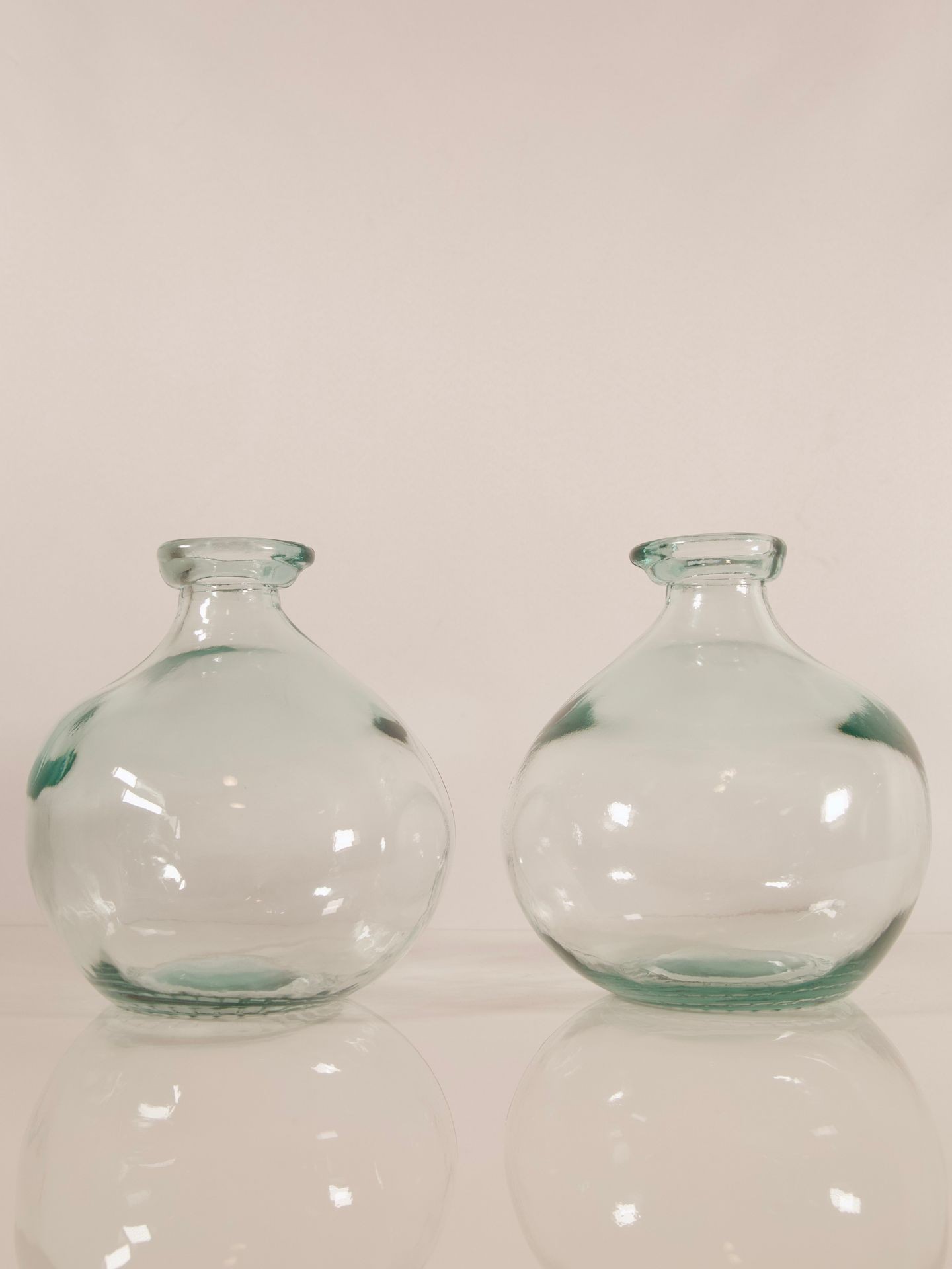 Two clear glass vases with round shapes placed side by side against a plain background.