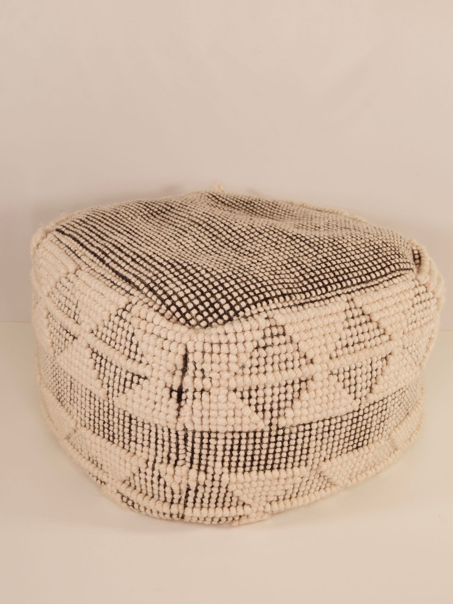 A textured, cube-shaped knitted pouf with a geometric black and white pattern.