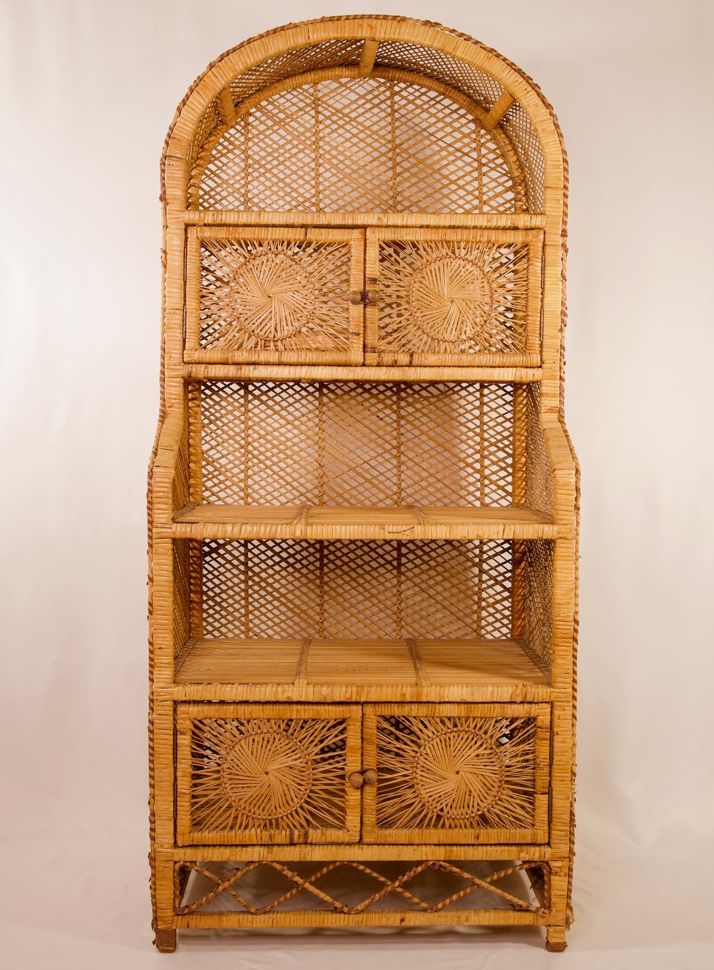 Tall rattan bookshelf with two drawers at the bottom and arched top on a light background.