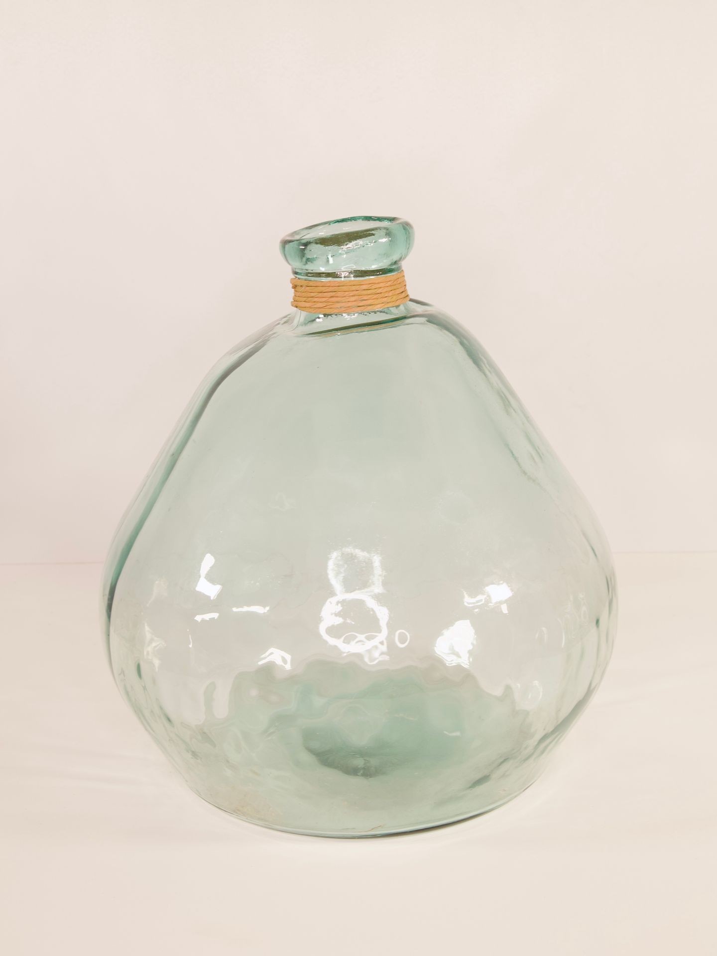 Transparent glass bottle with a round base and short neck, featuring a small band around the neck.