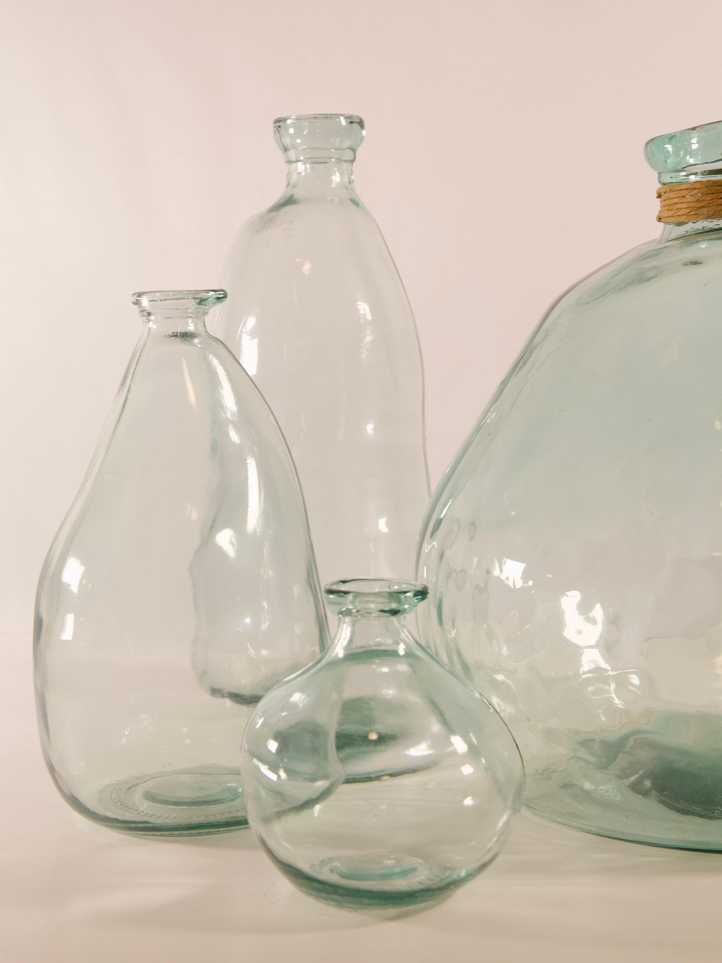 Collection of clear, empty glass bottles of various shapes and sizes against a plain background.