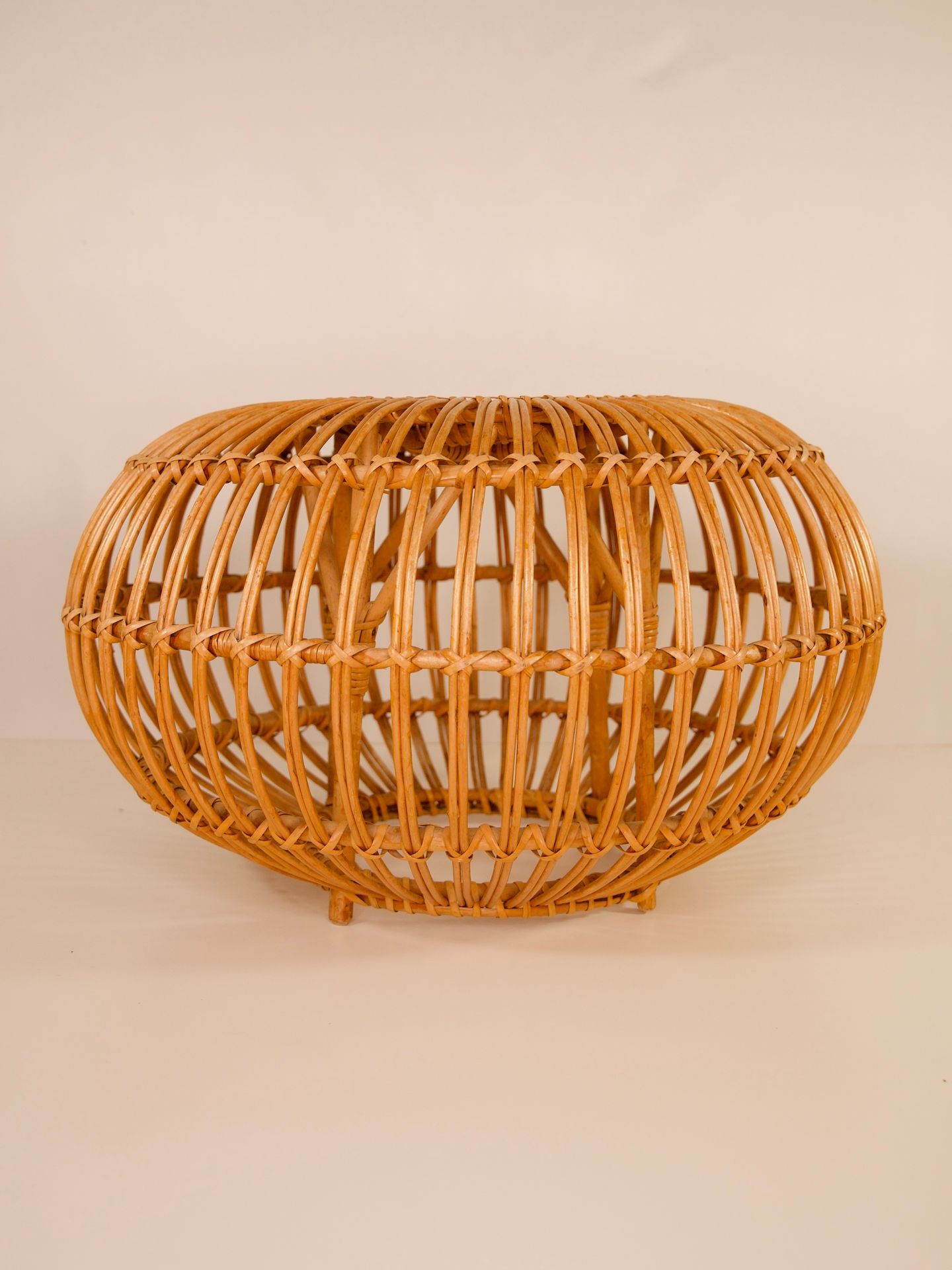 Round wicker basket with a natural wood finish against a plain beige background.