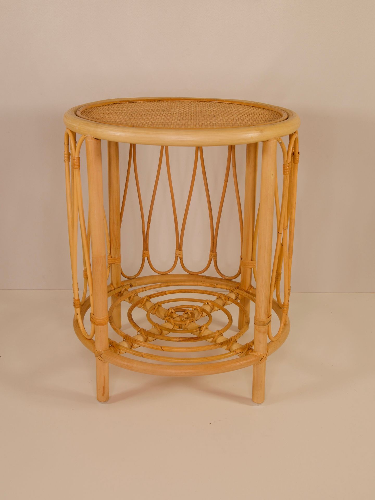 Round wicker side table with an open cylindrical frame and woven top and base in natural wood color.