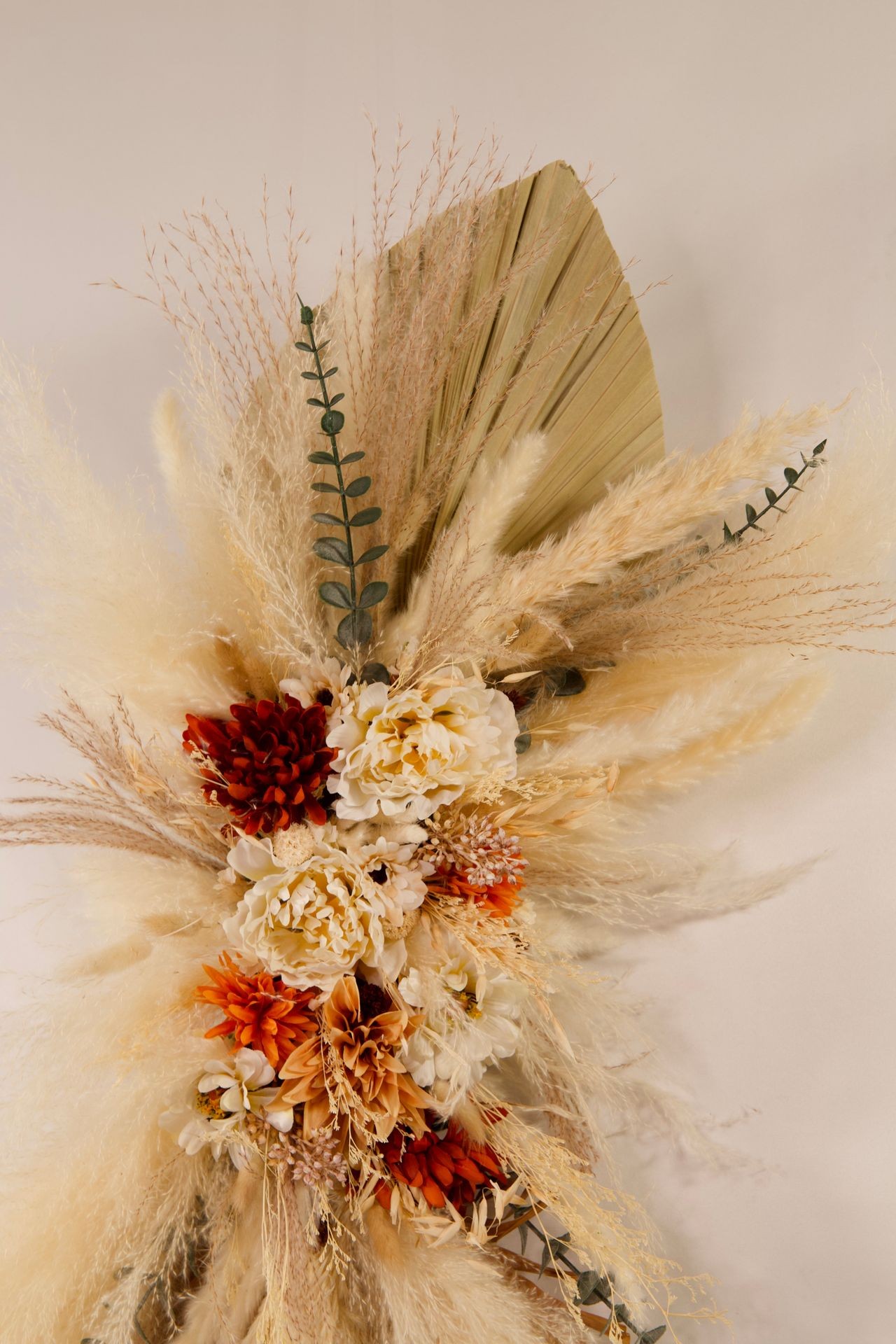 Elegant arrangement of dried pampas grass with white and orange flowers against a light background.