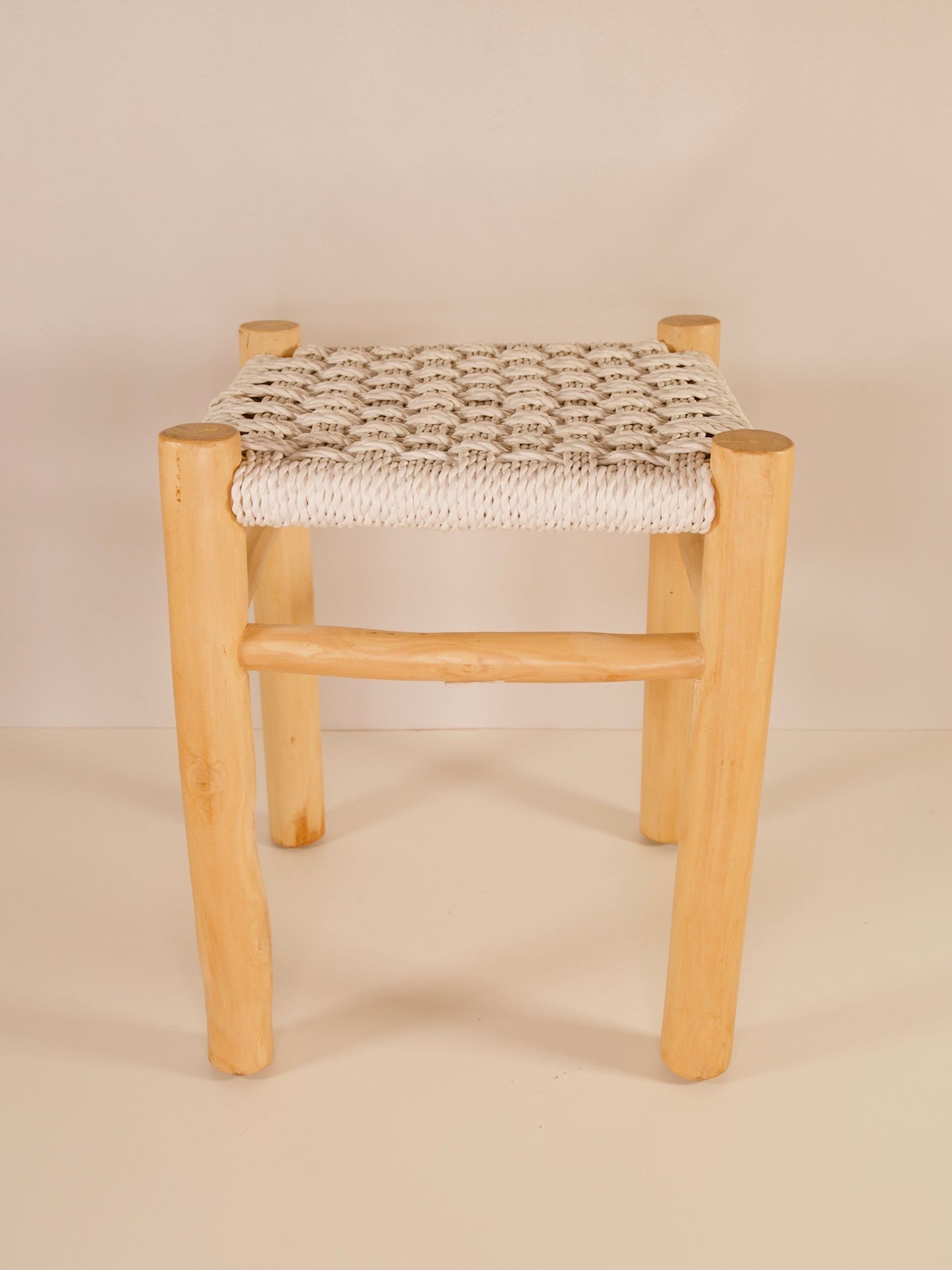 Handmade wooden stool with a woven seat placed against a plain background.