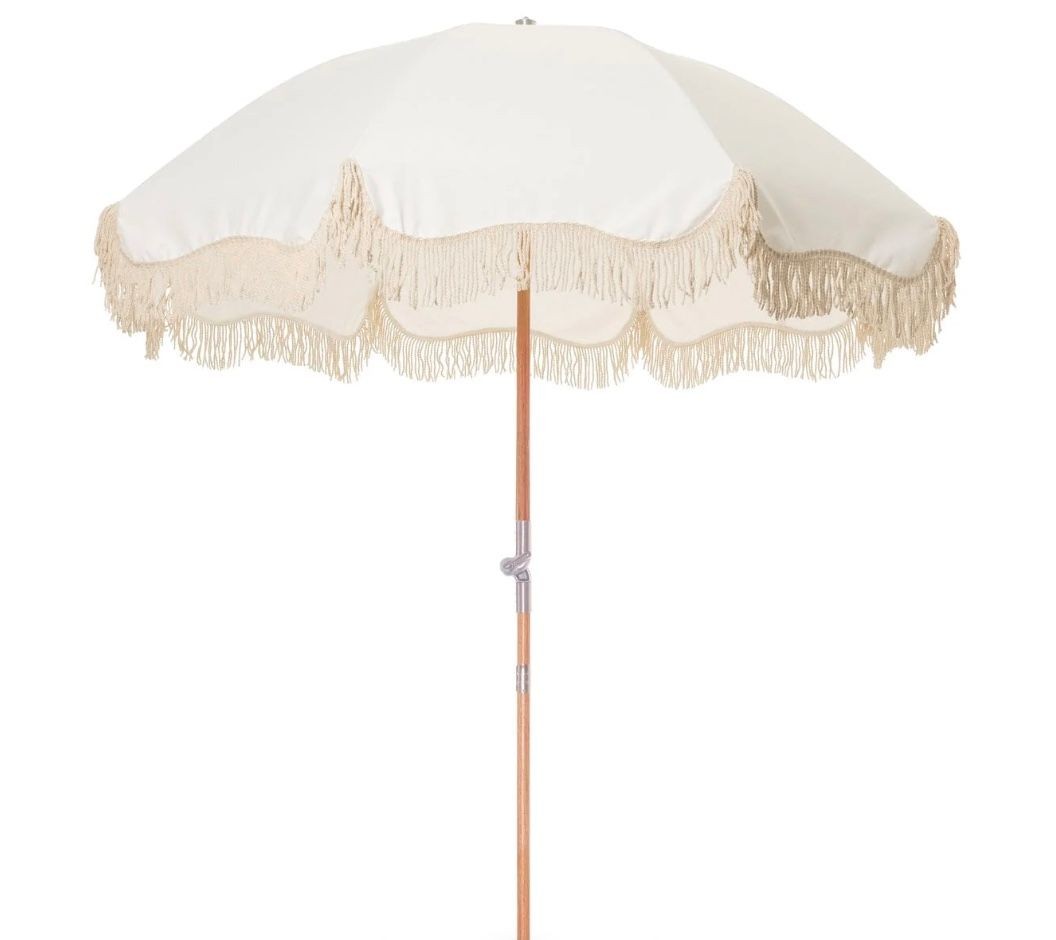 White patio umbrella with beige fringe trim on a wooden pole, isolated on a white background.